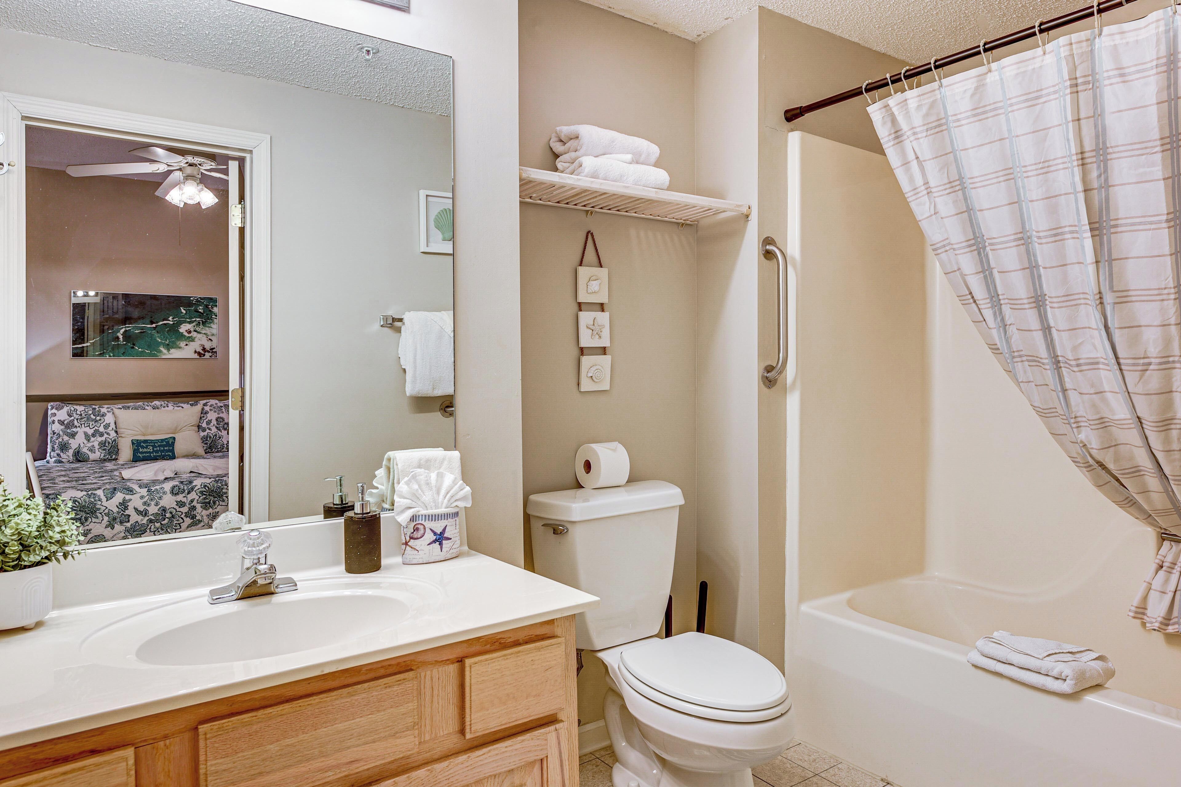 Une salle de bain équipée d’un lavabo, de toilettes et d’une baignoire. On y trouve un porte-serviettes avec des serviettes et un rideau de douche.