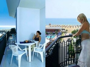 Un balcón con mesa y sillas, con vista a una piscina y una zona de playa.