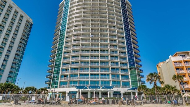 A multi-story hotel with a curved facade, balconies, and a pool area with sun loungers. - Sky-High Oceanfront Retreat – 21st-Floor Penthouse (Myrtle Beach)