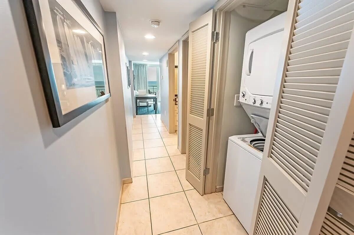 Um corredor com chão de azulejos, um quadro na parede e uma área de lavanderia com máquina de lavar e secadora.