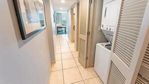 A hallway with a tiled floor, a framed picture on the wall, and a laundry area with a washing machine and dryer. - Sky-High Oceanfront Retreat – 21st-Floor Penthouse (Myrtle Beach)