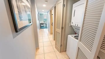Um corredor com chão de azulejos, um quadro na parede e uma área de lavanderia com máquina de lavar e secadora.