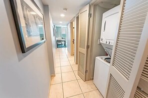 A hallway with a tiled floor, a framed picture on the wall, and a laundry area with a washing machine and dryer. - Sky-High Oceanfront Retreat – 21st-Floor Penthouse (Myrtle Beach)