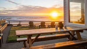 Een houten terras met picknicktafels en stoelen met uitzicht op de oceaan bij zonsondergang.