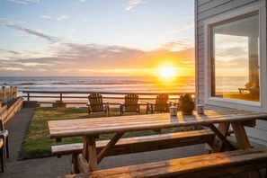 Eine Holzterrasse mit Picknicktischen und -stühlen mit Blick auf den Ozean bei Sonnenuntergang.