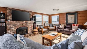 Een woonkamer met een open haard, een televisie en uitzicht op de oceaan.