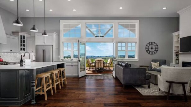 A modern kitchen with a large island, wooden stools, and a view through the open door to a dining area with a table and chairs. - The Quandary Vineyards Estate (Yamhill)