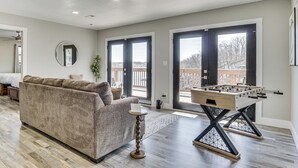 A living room with a sofa, a foosball table, and a large window. - Private Dock & Theater Room: Lake Ozark Luxury (Lake Ozark)