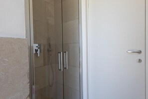 A glass-enclosed shower with a control panel, a white door with a handle, and a tiled wall. - Le Lamie di Minerva Bianca (Ostuni)