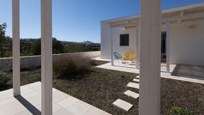 Un espace patio extérieur moderne, avec un bâtiment blanc, un mur de pierre et une vue sur la ville en arrière-plan.