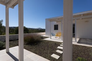 A modern outdoor patio area with a white building, a stone wall, and a view of the city in the background. - Le Lamie di Minerva Bianca (Ostuni)