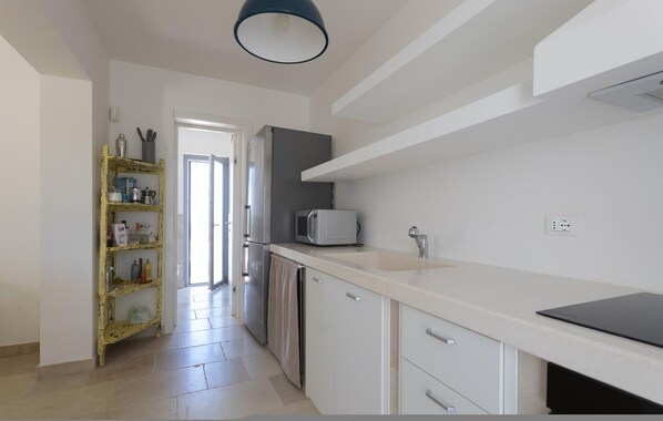 A modern kitchen with white cabinets, a grey refrigerator, a microwave, and a black countertop. - Le Lamie di Minerva Bianca (Ostuni)