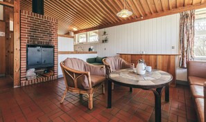 Een knus vertrek met een bakstenen open haard, rieten stoelen, een ronde tafel met een waterkoker, en houten balken aan het plafond.