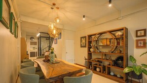 Een eetruimte met een grote houten tafel, zes stoelen, een kroonluchter en een decoratieve boekenkast.