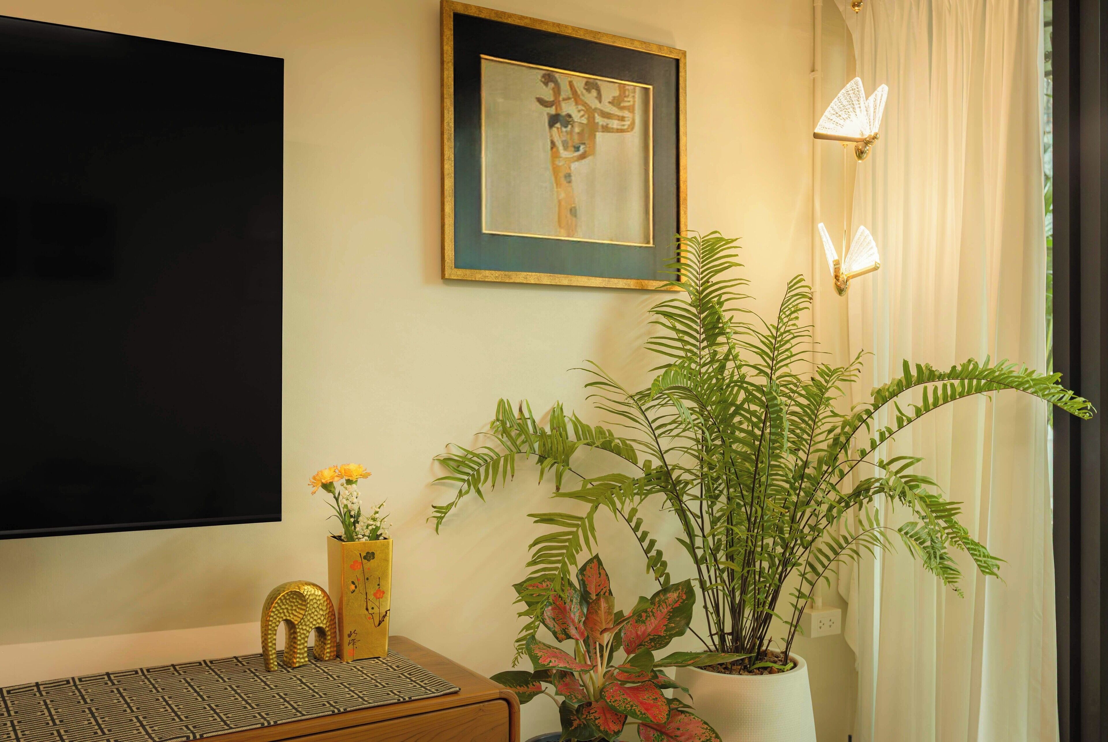 Quarto com televisão de tela plana, obra de arte emoldurada, planta em vaso e um vaso decorativo com flores.