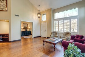 A spacious living room with hardwood flooring, a glass coffee table, a red sofa, and a large window with blinds. - Fairfield Wine Country Getaway w/ Backyard Oasis! (Fairfield)
