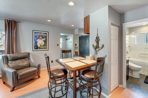A living room with a leather sofa, a wooden dining table with four chairs, and a poster on the wall. - Hike, Bike & Ski! Cozy Anchorage Townhome (Anchorage)