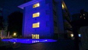 A building with a pool area at night, illuminated by blue lighting. - Studio with air conditioning, balcony and pool (Bibione)