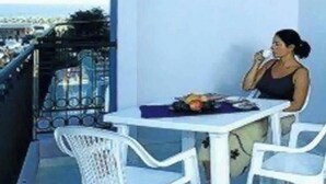 A balcony with a white table and chairs, a person sitting, and a view of the city. - Studio with air conditioning, balcony and pool (Bibione)