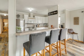 A modern kitchen with white cabinets, a bar area with grey barstools, and a wooden floor. - Lake Conroe Bliss: Waterfront Home w/ Boat Ramp (Willis)