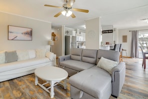 A modern living room with a white sofa, grey sectional, and a small white table. A ceiling fan and a painting are visible. - Lake Conroe Bliss: Waterfront Home w/ Boat Ramp (Willis)
