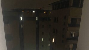 Ein Balkon mit Blick auf ein Gebäude mit zahlreichen Fenstern. Auf ihm steht ein kleiner runder Tisch mit Mosaikplatte.