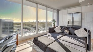 A modern living room with a large window, a sofa, and a minimalist design. - Elegant Condo w/ Stunning Views in Dtwn Hollywood (Hollywood)