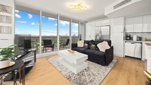 A modern living room with a black sofa, white coffee table, and a city view through large windows. - Elegant Condo w/ Stunning Views in Dtwn Hollywood (Hollywood)