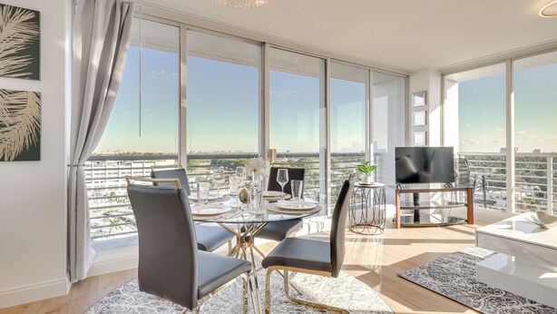 A modern living room with a dining area, large windows, and a view of the city. - Elegant Condo w/ Stunning Views in Dtwn Hollywood (Hollywood)