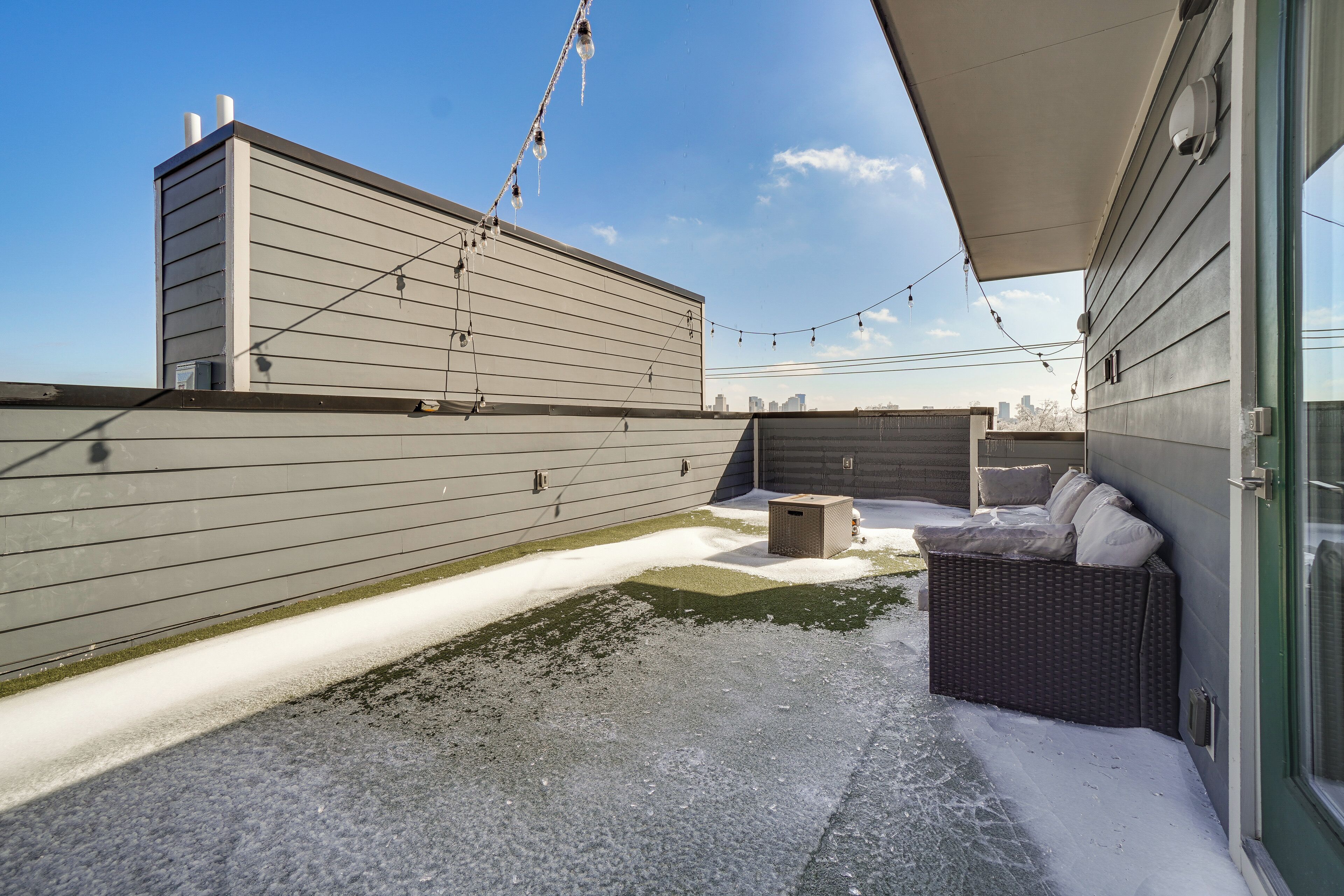 A rooftop patio with a covered seating area, a small trash bin, and a clear view of the city skyline.