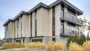 Un edificio de varios pisos con fachada de piedra, balcones y un área ajardinada con pasto seco.