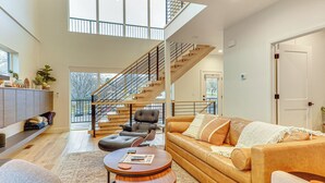 Un salón espacioso con techos altos, una escalera, un sofá, una mesa de centro y vistas al exterior.