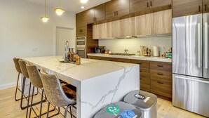 Una cocina moderna con una isla central, taburetes de bar, electrodomésticos de acero inoxidable y armarios de madera.