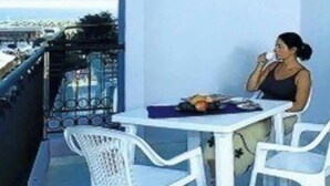 A balcony with a white table and chairs, a person sitting, and a view of the city. - Studio with air conditioning, balcony and pool (Bibione)