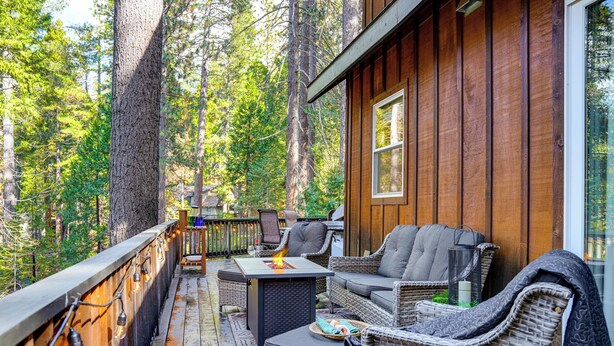 A wooden deck with wicker furniture, a fire pit, and a view of a forest. - Game Room & Hot Tub! Dog-Friendly Arnold Retreat (Arnold)