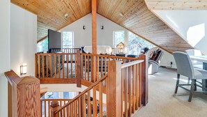 A spacious loft with a high ceiling, wooden beams, a cozy seating area, and large windows offering views of the outdoors. - Game Room & Hot Tub! Dog-Friendly Arnold Retreat (Arnold)