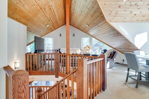 Ein geräumiges Loft mit hohen Decken, Holzbalken, einer gemütlichen Sitzecke und großen Fenstern mit Blick ins Freie.