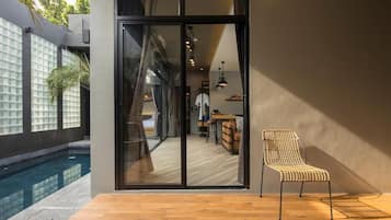 A modern interior with a glass door leading to a pool area, a wooden deck, and a wicker chair.