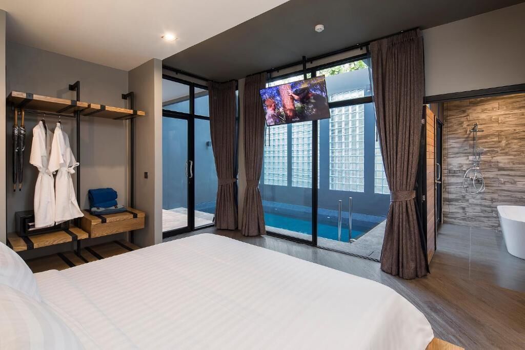 A modern hotel room with a large bed, a TV, a balcony with a pool view, and a separate bathroom with a shower.