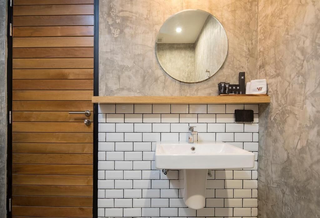 A bathroom with a wooden door, a white sink with a mirror above it, and a shelf with toiletries.