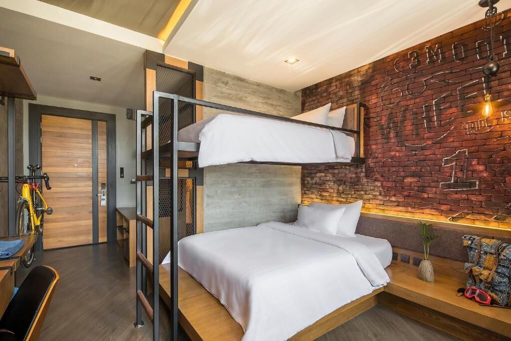 A modern hotel room with a bunk bed, a wooden desk, and a brick wall with graffiti.