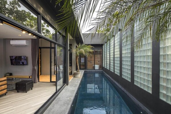 A modern indoor pool area with glass walls, a bench, and a television. - Wheeler Bed & Bike (Chonburi)