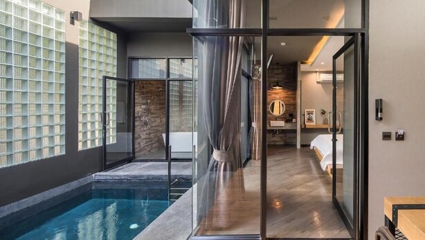 Une chambre d’hôtel moderne dotée d’une porte en verre donnant accès à une salle de bain, à une piscine et offrant une vue sur l’extérieur.