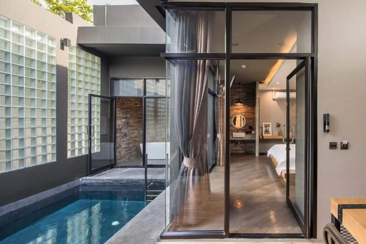 Habitación de hotel moderna con puerta de vidrio que da a un baño, una piscina y vistas al exterior.