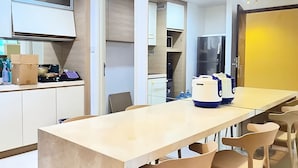 A modern kitchen with a central island, wooden chairs, and a long dining table. - Casa By SanLiving - 2BR - Kasablanka (Jakarta)
