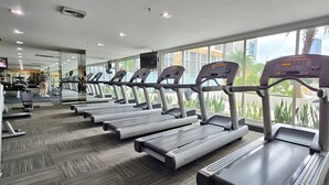 A gym with treadmills aligned in rows, large windows, and a TV screen. - Casa By SanLiving - 2BR - Kasablanka (Jakarta)