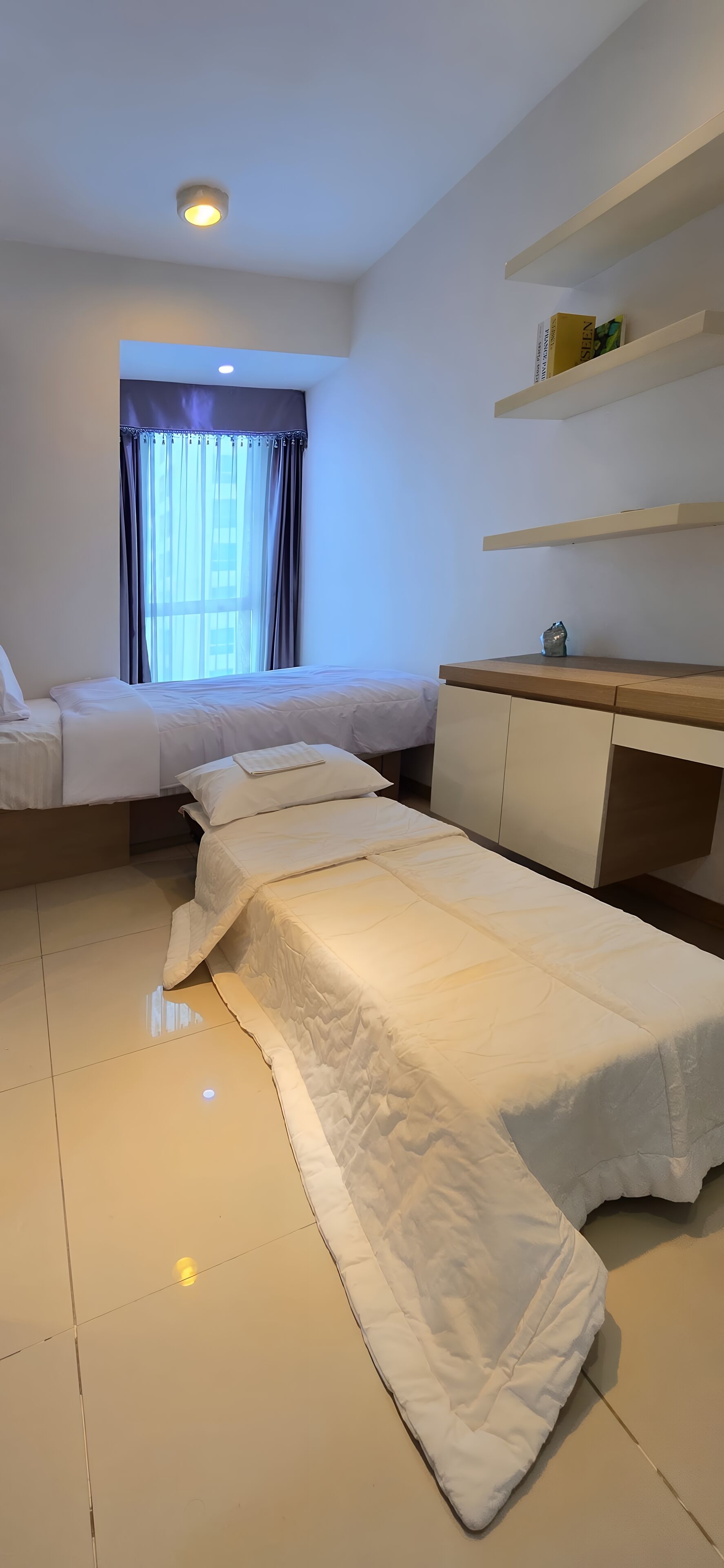 A modern hotel room with a large bed, a bedside table, a desk, and a window with curtains.