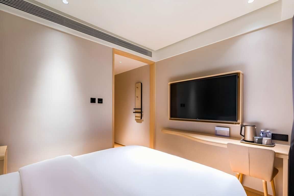 A hotel room with a bed, a TV mounted on the wall, a desk with a coffee maker, and a mirror.