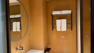 A compact bathroom with a wooden wall, a large mirror, a sink, a toilet, and a towel rack.