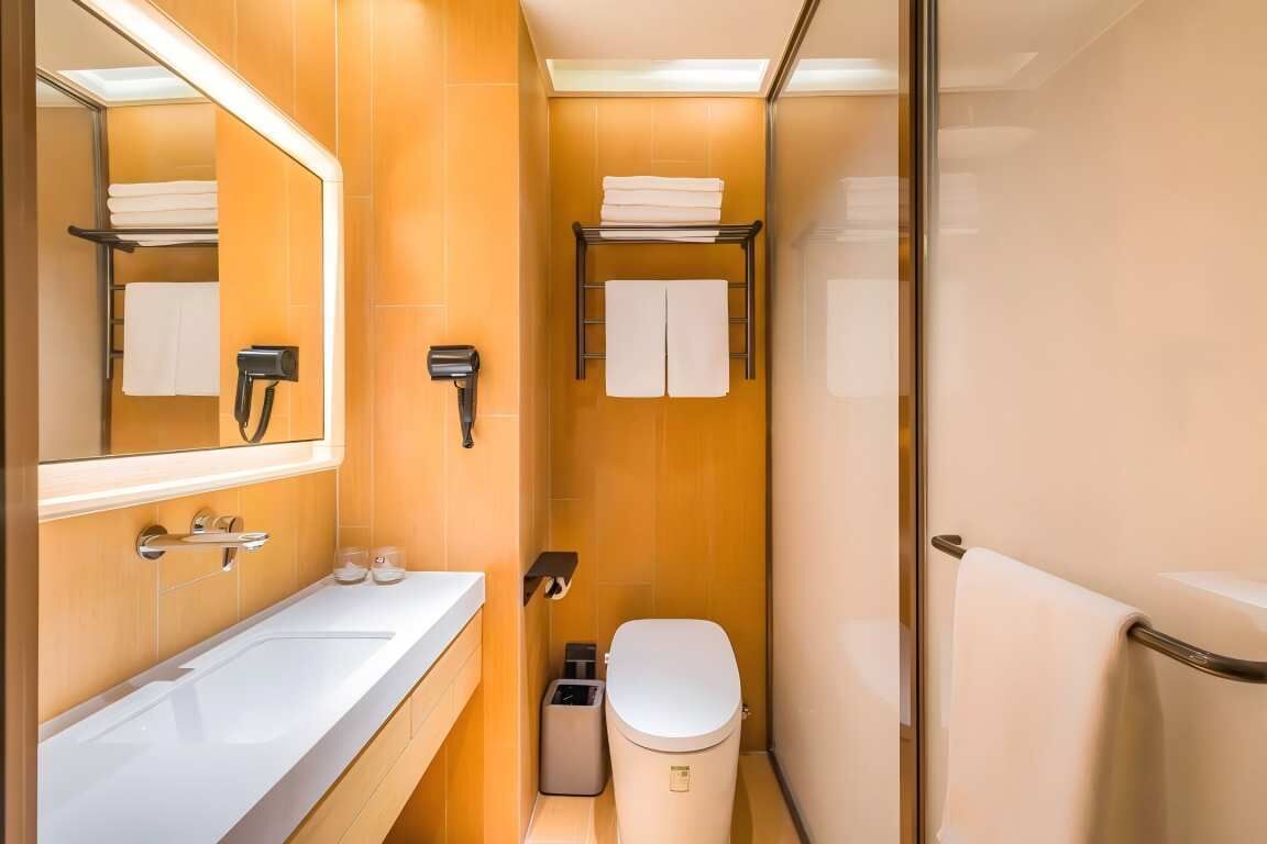 A compact bathroom with a white sink, a toilet, and a glass shower enclosure.